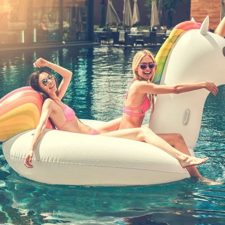 Deux jeunes femmes sur une bouée en forme de licorne dans une piscine