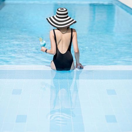 Jeune femme avec chapeau assise au rebord d'une piscine