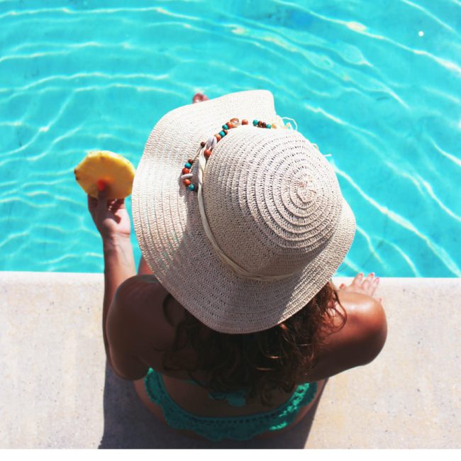 Jeune femme avec chapeau au bord d'une piscine